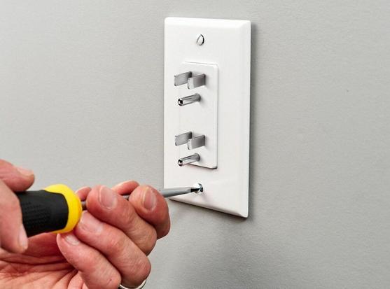 A picture of a hand holding an insulated screwdriver and turning a screw on a wall plug. The hand is grasping the shaft of the screwdriver and not at all paying attention to how many fingers and thumbs it has touching the non-insulated part of the tool.