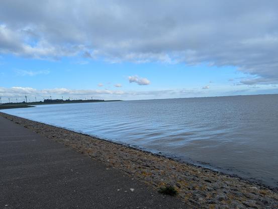 Rechts im Bild ist die Nordsee. Direkt an der Wasserkante sieht man einen Weg.
im Hintergrund am Horizont ein paar Windräder.