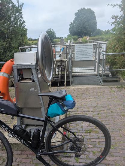 Ein Fahrrad lehnt an einer Kurbel für eine handbetriebene Personenfähre. 
Die Personenfähre liegt an.
