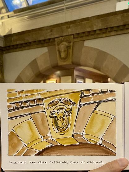 An Arch with the head of a bull, carved from stone, in the foreground a Sketchbook with a coloured sketch of that scene.