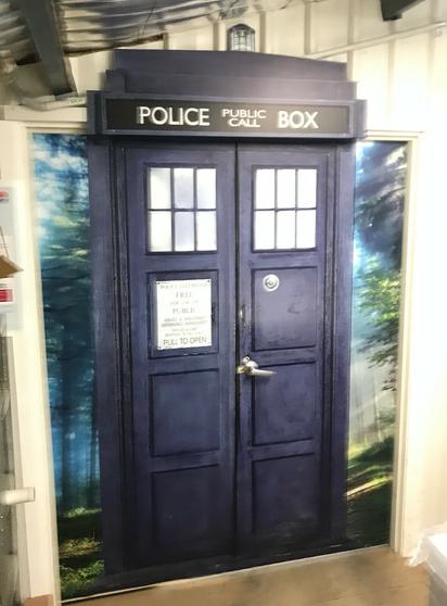 A photo of tardis doors into a workroom in a print factory. The tardis is wrapped onto the door so the door handle and split down the middle opens in the correct place, and the upper Police Box signage is created from panels above the door.