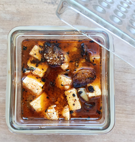 in einer viereckigen Glasschale der eingelegte Feta wie beschrieben. Der Glasdeckel ist an die Schale gelehnt.