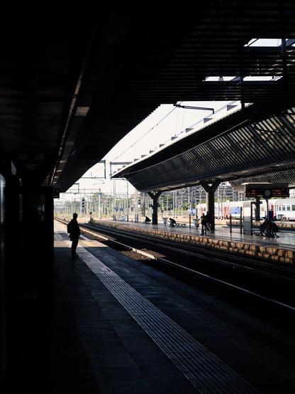 A man waits for the train on a station platform. Sunlight comes from the opposite side, creating a silhouette of the man.