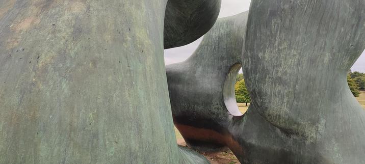 a large, weathered bronze sculpture of flowing curves with s circular hole.