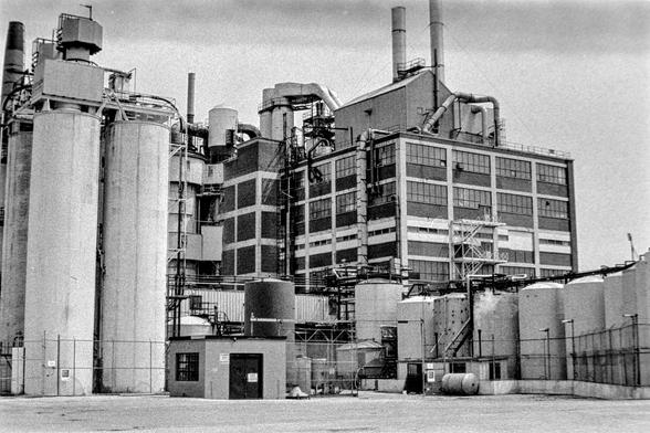 black and white photo of multi storey factory with storage tanks in foreground