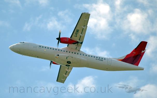 Side view of a high-winged, twin propellor-engined airliner flying from right to eft at a very low altitude, with the undercarriage already stowed away, flaps extended from the rear of the wing, and the nose raised sharply, suggesting it has just taken off.
The plane is almost entirely white, with only the black registration "G-PEMB" on the lower rear fuselage and under the left wing outboard of the red engine pods.
The tail has a pair of over-lapping red stripes, getting darker where they cross.
Pale blue sky with fluffs of white cloud fill the rest of the frame.