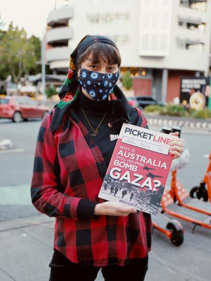A wonderful comrade from Brisbane holding a copy of picket line, it says "Why is Australia helping bomb Gaza" and looks pretty high quality!

The comrade has a lot of evil eyes on their mask.