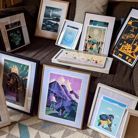 Photo of a sofa laden with picture frames with my art prints in them. Some of them have new prints in front of them, waiting to be changed.