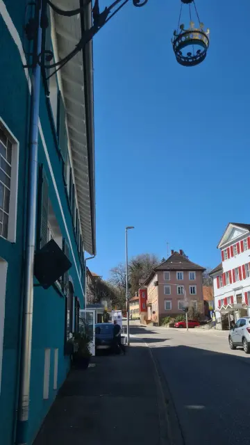 #hegaubodensee #hegauliebe  #singenhohentwiel
 
 
petrolfarbenes Gebäude Krone Randegg, sonniger Blick die Längsseite entlang nach oben zur Krone am Gebäude, zum Himmel hoch ins weitere Dorf die Straße entlang