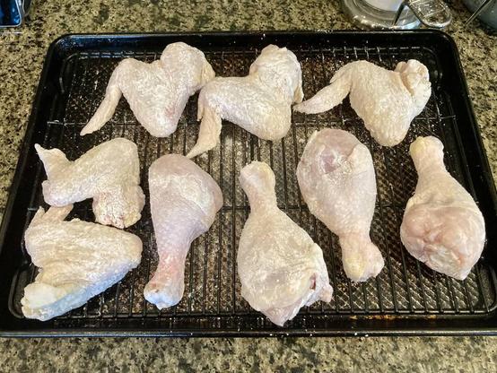 A photo of several raw chicken wings and drumsticks on a wire rack in a sheet pan.