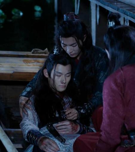 In a boat by Lotus Pier, an unconscious Jiang Cheng is slumped against Wei Wuxian with Wen Ning, shown from behind on the right side of the image, sitting nearby toward the other end of the boat. Jiang Cheng is bedraggled, and splotched with blood on the back of his hands and by his mouth. Wuxian has his arms around Jiang Cheng as he looks down at the other with a distressed expression.