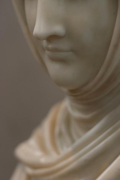 A closeup of a marble statue of a woman, an amazing piece with beautiful subtle details. Her lower face is in focus, while her robes fade into blur in the distance.