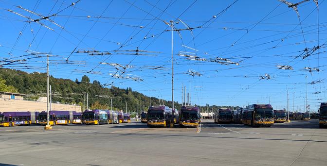 king county metro atlantic base parking lot with a bunch of trolleybuses and a web of trolley wires above