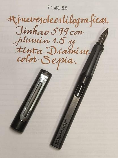Una estilográfica Jinhao 599 con el capuchón quitado que muestra el plumín clásico, diferente del de Lamy y el clip plano con una ranura central hecho con una lámina metálica. Escrito, La marca y modelo y anchura del plumín y la tinta (Diamine Sepia)