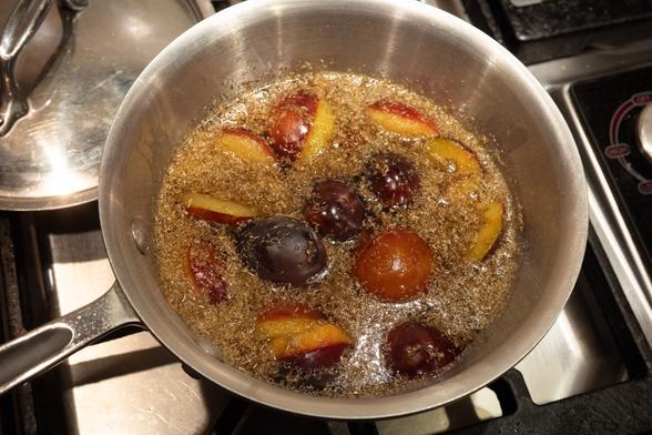 Stainless steel pot with halved plums bobbing in a liquid covered with bits of tea.