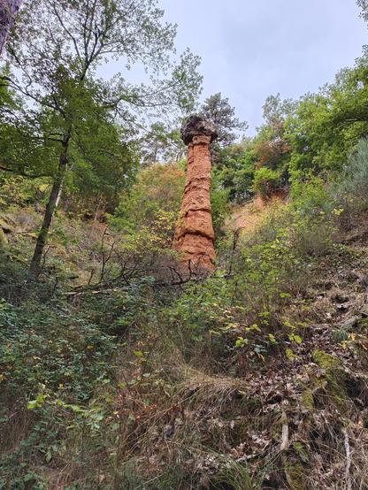 4 photos numériques couleur de différents formats, avec une vue en contre-plongée, dans un relief escarpé, d'une sorte de cheminée dont le corps est de couleur ocre et dont le sommet est une pierre grise. De la végétation autour et un ciel bleu pâle.