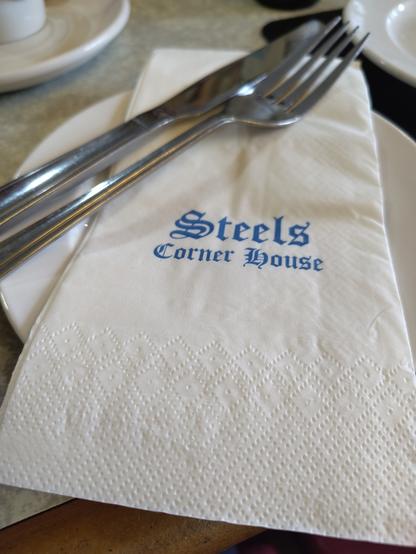 A photo of a white paper napkin on a table, printed with the words Steels Corner House in a gothic typeface