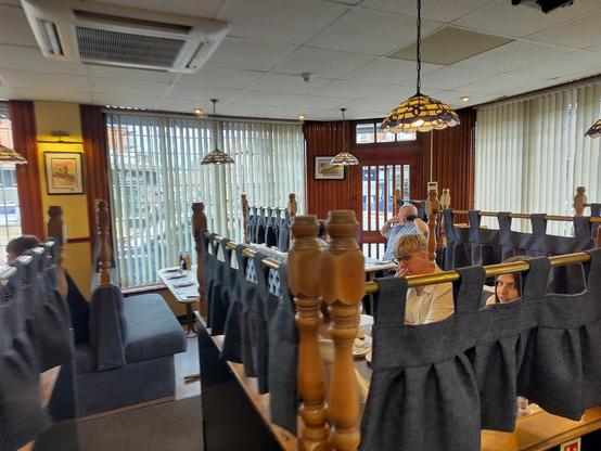 A photo of some traditional looking booths inside a fish chip restaurant. Each booth is made of wood surrounds with blue heavy material drapes separating each booth