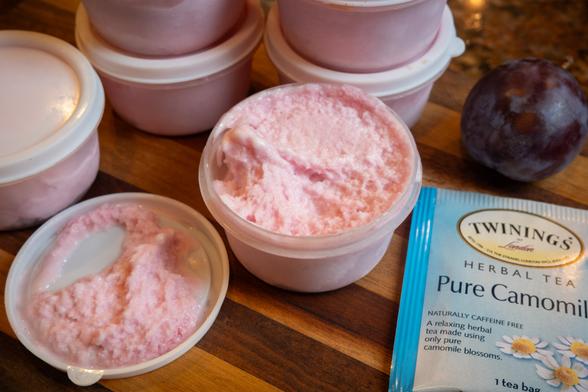 Small plastic container filled with pink fluffy sorbet. Nearby is a plum and a packet of tea, plus some other containers that are closed and ready to be stored in the freezer.