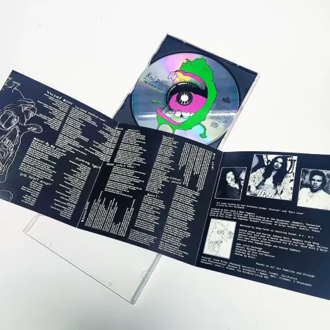 A CD copy of Meat Puppets' 1994 LP Too High to Die with its case open so you can see the green monster art on the CD itself, and the booklet is showing its interior with lyrics, art and photos of the band.