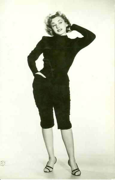 Retrato de Evangelina Elizondo posando con una mano en la cabeza y la otra en la cadera, vestida con un atuendo negro y tacones, en un fondo blanco.