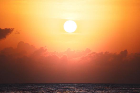Una vibrante puesta de sol sobre el océano, con un gran sol en el centro, rodeado de cálidas nubes naranjas y rosadas, que se reflejan en la superficie del agua.