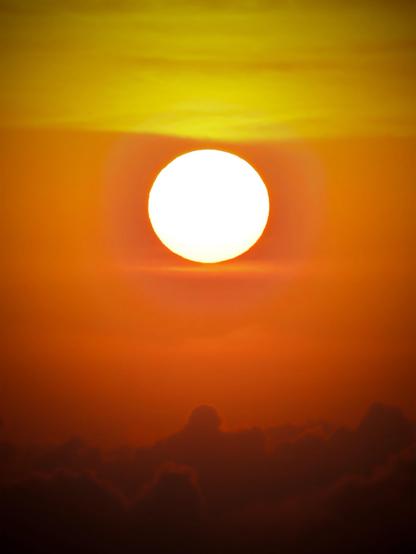 Una vibrante puesta de sol con un sol grande y brillante rodeado de capas de cielos naranjas y amarillos, recortado contra suaves nubes.