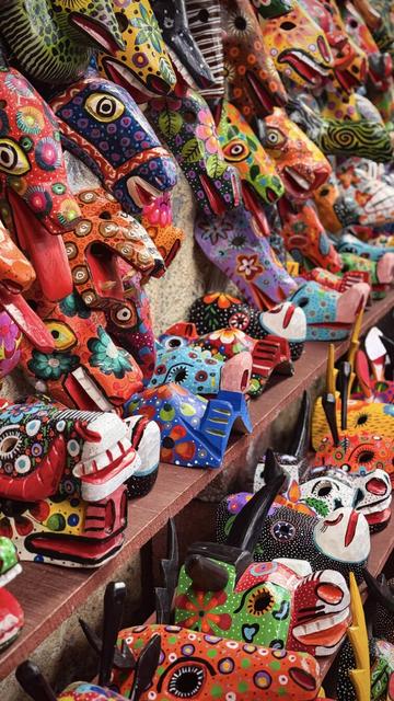 A collection of vibrantly colored carved wooden masks in the shape of various animals.