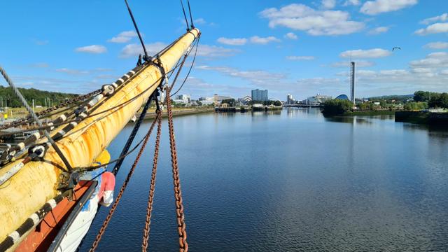 Looking past the bowsprit of a tall ship to the modern buildings of Glasgow's waterfront.