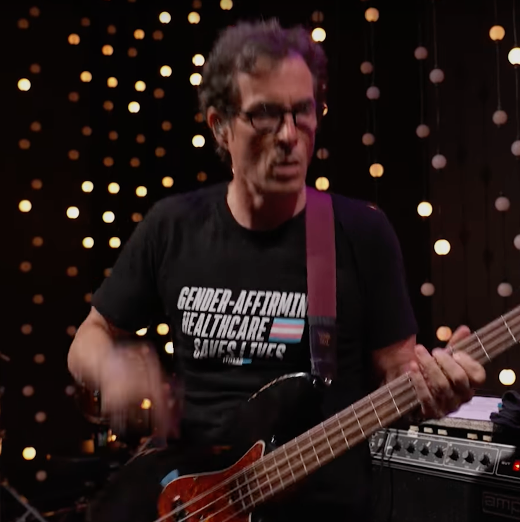 a picture of the bassist wearing a t-shirt that says "Gender affirming healthcare 🏳️‍⚧️ saves lives"