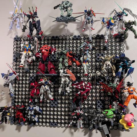 A cacophany of wall-mounted Bandai model kits on something similar to a pegboard. Most are in a flying pose, with one on a 3D printed shelf.