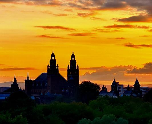 The spires of Kelvingrove Art Gallery against an orange and gold sunset.