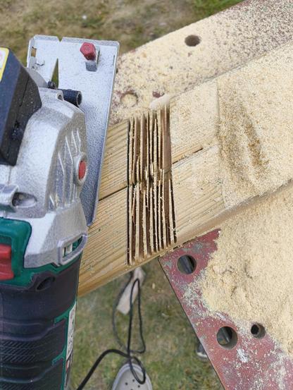 Zwei Holzbalken sind zusammen gezwungen und auf einer Breite von 4,5cm immer wieder eingesägt. Die so entstandenen feinen Lamellen lassen sich nun einfach herausbrechen. Neben der Schnittstelle liegt eine kleine Handkreissäge. Die Werkbank unter dem Holz ist mit Massen von Sägemehl bedeckt.