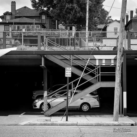 A two level garage with stairs leading to the second level from the sidewalk.  Several cars are parked on the lower level.