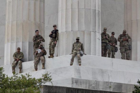 Eight national guard troops looking insignificant next to a marble column that is thicker than all of them combined. The sitting ones look like children with their legs dangling down the giant steps.