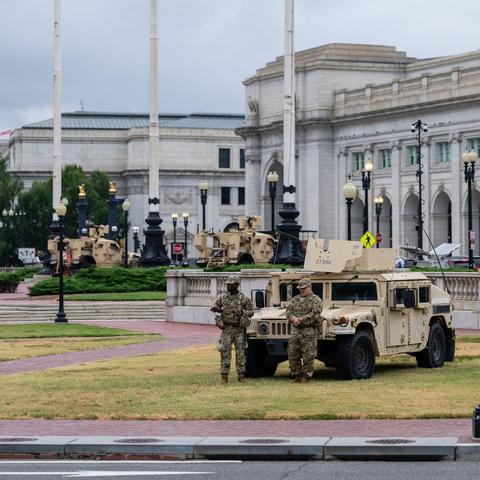 Two national guard troops with a humvee stationed in front of a government building. They look small and absolutely no one else is around.