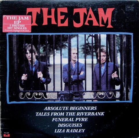 The cover of The Jam EP: on a black background, "The Jam" is at top in thick, mid-century style font in red. Across the middle, a  photo of the three band members behind iron grating gate. Below the five tracks discussed in the post are listed in white. At upper left, a red sticker proclaims "The Jam EP - 5 British hit singles previously unreleased in the U.S.A."