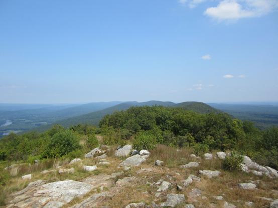 View from a ridge, looking down the length of it. There are some rocks nearby, and everything in the distance is green.