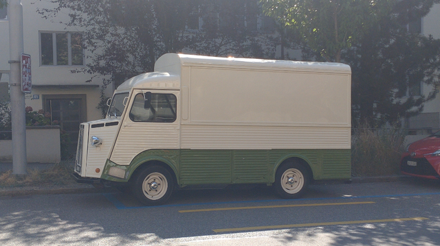A cream white and moss green Citroën HY delivery van from the '60s with corrugated side panels, high roof and rear extension parking at the side of the street.