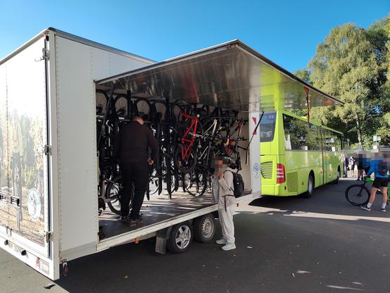 A trolley full of bikes, back a green buss. The side door to the trolley is open.