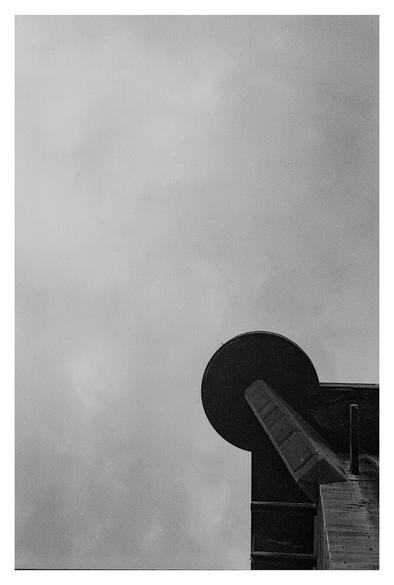 Black-and-white photograph taken in Augarten Park in Vienna. The lower right quarter of the image shows a corner of the control tower, which together with the combat tower forms Flakturmpaar VII, one of three such pairs in Vienna. The remaining three quarters of the image show a cloudy sky.