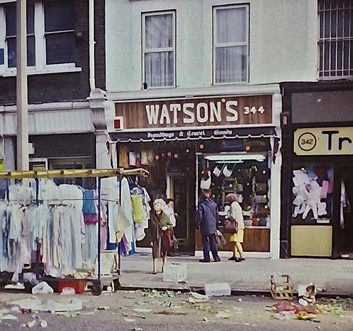 Street scene, with the 'WATSONS' shop partially obscured by a market stall. Lots of rubbish in the gutter.