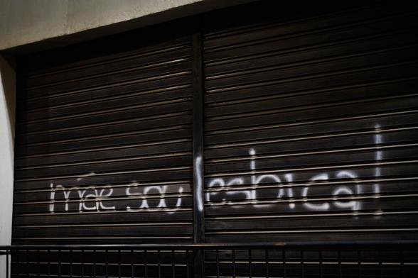 Pixação escrito "mãe sou lésbica!" em letras brancas em uma porta de enrolar de loja de cor preta, com um gradil também preto logo abaixo.