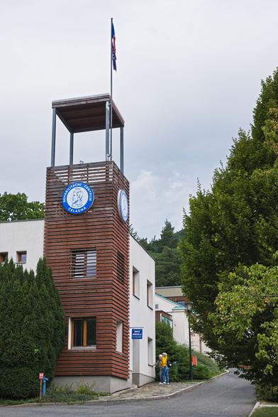 Vyvýšený roh budovy upravený jako rozhledna. Bílá budova, roh s rozhlednou obložen vodorovnými dřevěnými deskami.