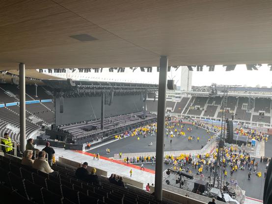 Kuva Olympiastadionin katsomosta ylhäältä kohti lavarakennelmaa, jonka edessä on huomattavan suuri määrä yleisöstä keltaisissa sadetakeissa. Katsomon katto ulottuu noin 30 m kuvauspaikkaa edemmäs.