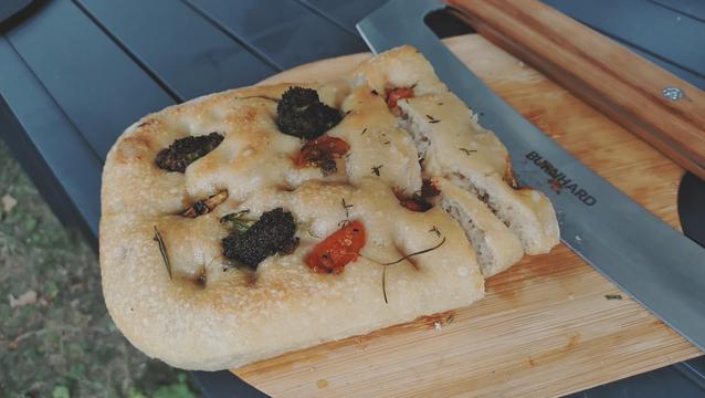 Focaccia mit Broccoli und Cherry - Tomaten auf einem Holzbrett mit einem großen Wiegemesser