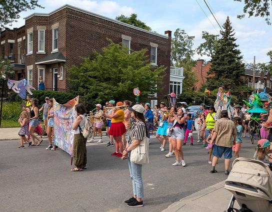 A parade with a brass band and a variety of costumes. Lot's of kids!