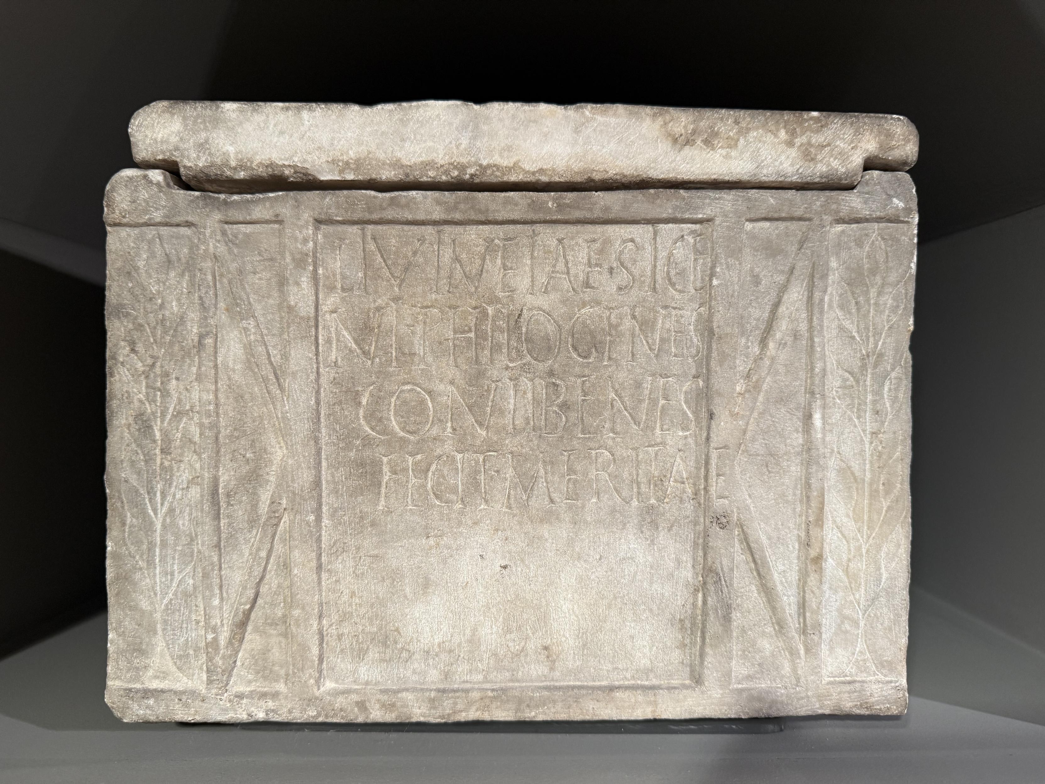 A Roman cinerary urn, bearing an inscription reading: LIVIAE SIBI NEPHIOGENES CONLIBERTAE FECIT MERITAE The very last E is outside of the space with the rest of the text, as the inscriber ran out of room.