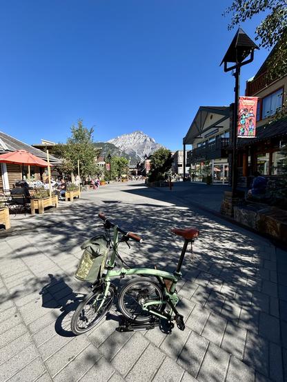 A green Brompton bike at Banff’s Woonerf (street where cars are guests) Bear Street. Cascade Mountain behind.