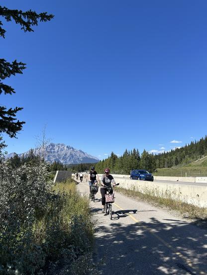 People on Bromptons riding the Legacy Trail from Banff to Canmore with Cascade Mountain behind.
